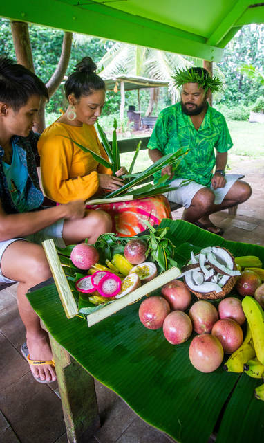 Teaching visitors to weave a kikau basket before a Tumunu, Atiu Island