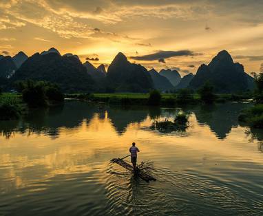 Een Aziatische man op een houten vlot met op de achtergrond het platteland in Ninh Binh.