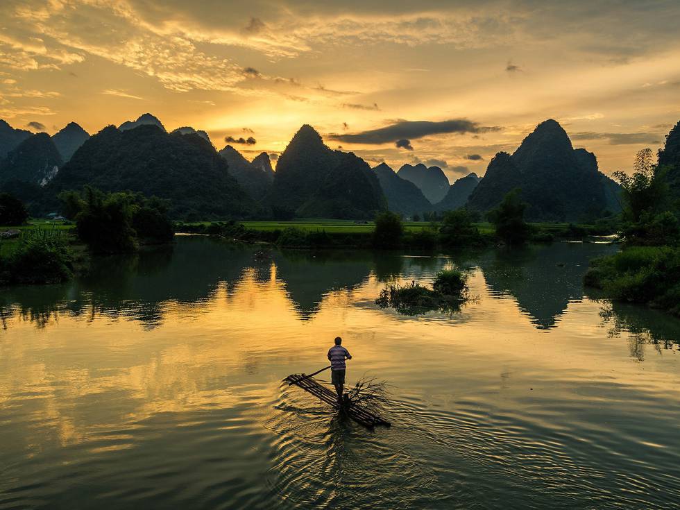 Een Aziatische man op een houten vlot met op de achtergrond het platteland in Ninh Binh.
