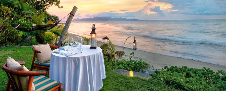 Een tafel met een kaars bij het Nanuku Auberge resort in Fiji met op de achtergrond de oceaan met ondergaande zon. 