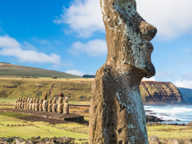 De Moai standbeelden op Paaseiland met op de achtergrond groene heuvels en de kust. 
