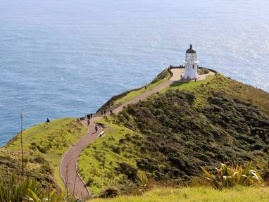 Groene heuvels met een witte vuurtoren tegen de blauwe zee bij Cape Reinga in Nieuw-Zeeland