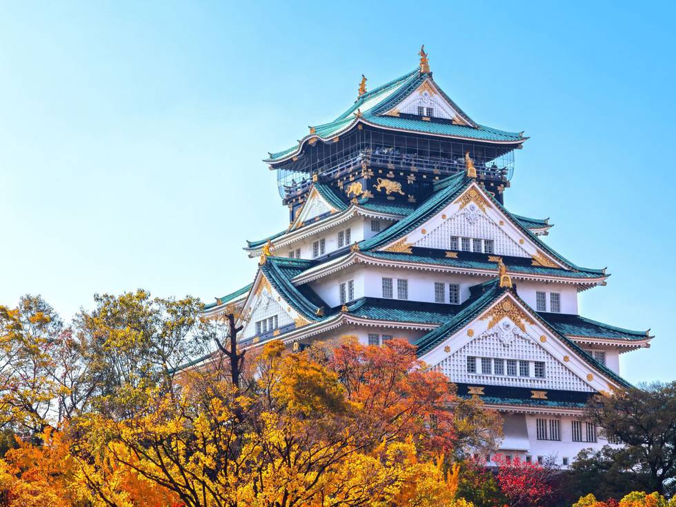 Een prachtige Japanse tempel met donkergroene dak en herfstbladeren er omheen. 