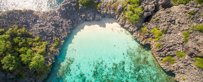 Een baai met helderblauw oceaan water en een wit strand vanaf boven gefotografeerd in Thailand.
