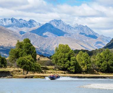 Een varende boot met op de achtergrond de bergtoppen van Glenorchy. 
