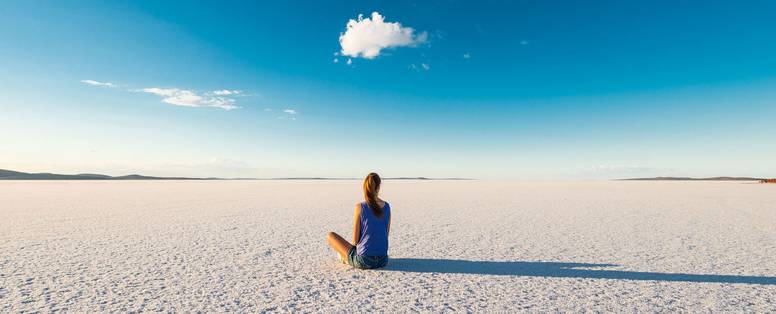 Een vrouw zit op een witte vlakte bij Lake Gairdner in Australië met een blauwe lucht. 