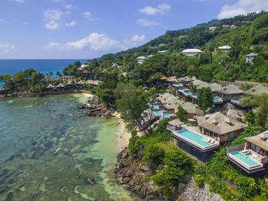 Villa's met zwembad aan de rand van de oceaan met groene bossen op de achtergrond. 