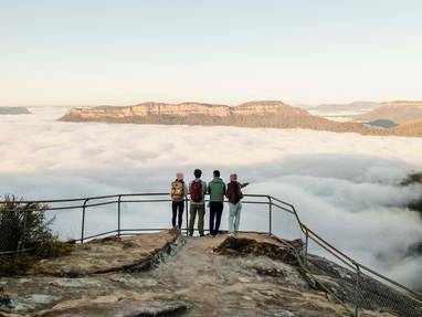 Drie personen kijken uit over blauwe bergen vanaf een richel op de Blue Mountains in Nieuw-Zeeland. 