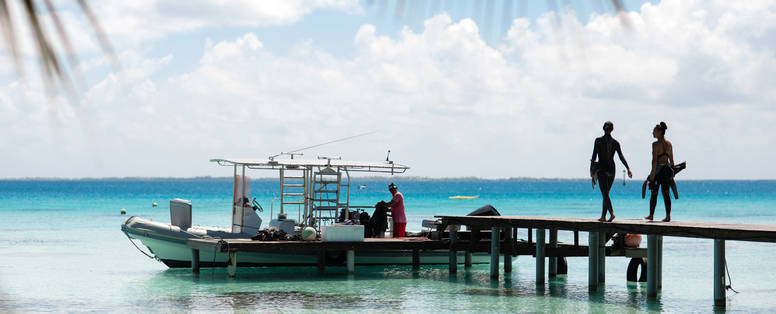 Een boot aangelegd bij een steiger in Frans-Polynesië en twee dames die over de stijger lopen. 