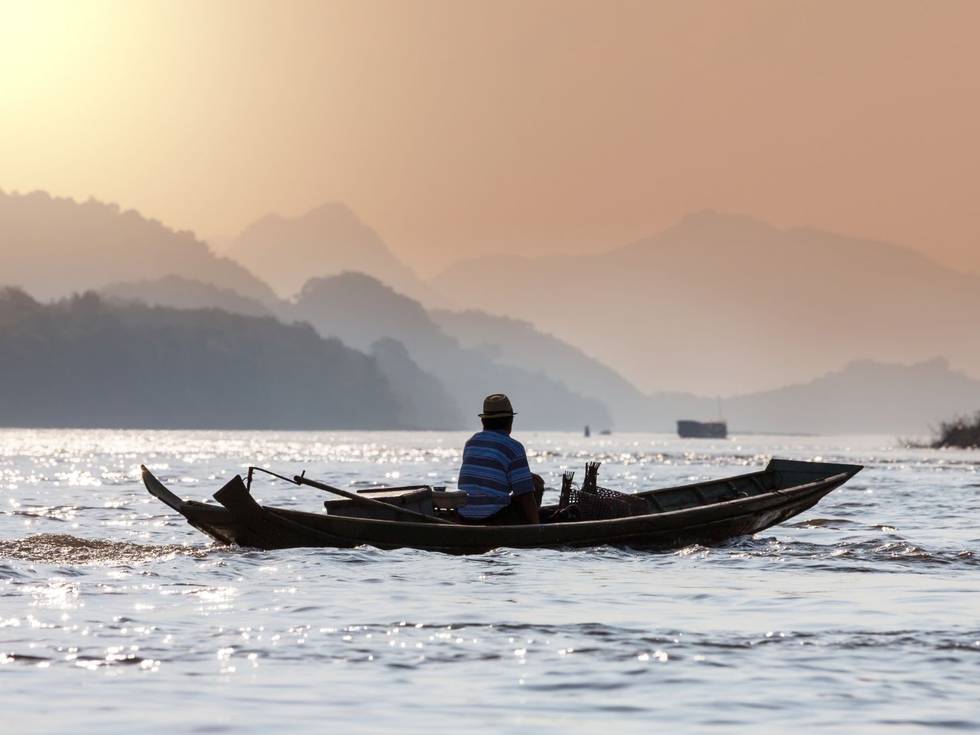 Een visser op een bootje in een meer bij Vang Vieng in Vietnam.