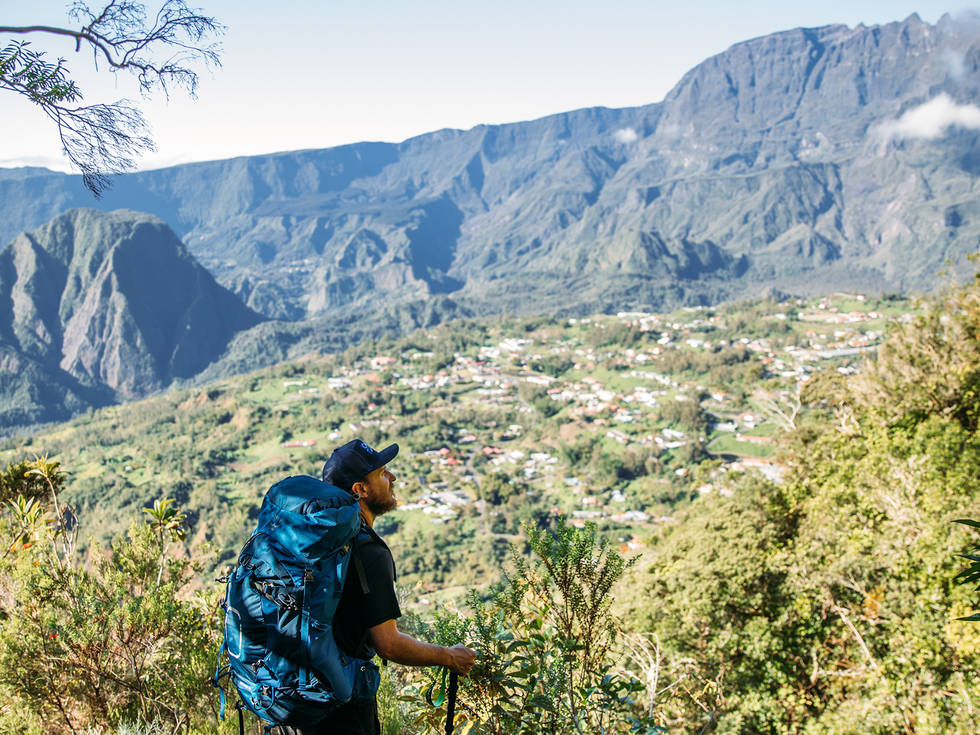 Een wandelaar met een grote rugzak op die aan de rand staat van een afgrond met uitzicht over de Mafate in La Reunion. 
